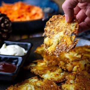 Parmesan Smashed Potatoes on a black plate with one being picked up about to be dipped in BBQ sauce.