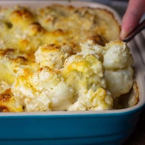 A spoonful of sourdough cauliflower cheese being taken out of a baking dish.