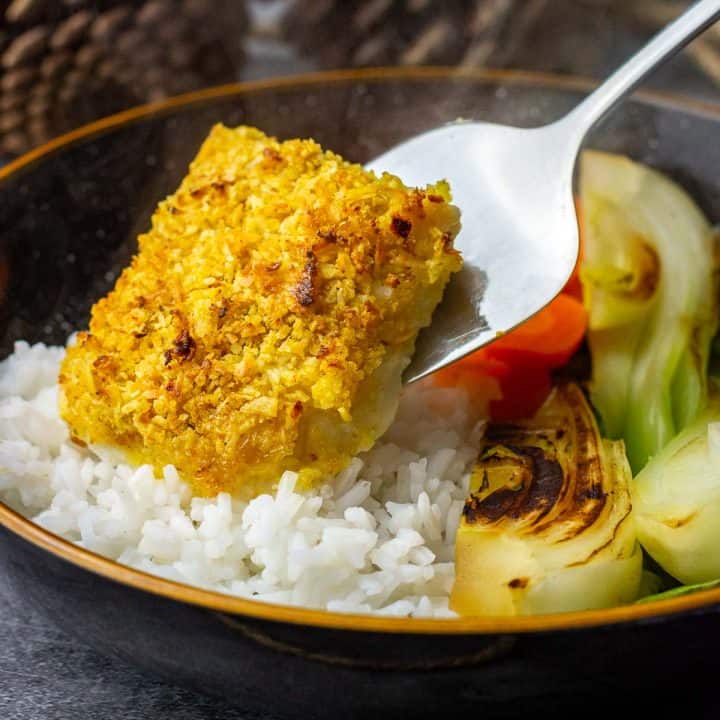 Baked coconut crusted cod being placed on a bed of rice.