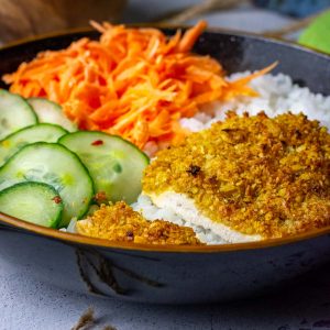 Baked Coconut Crusted Chicken breast on a bed of rice with vegetables.