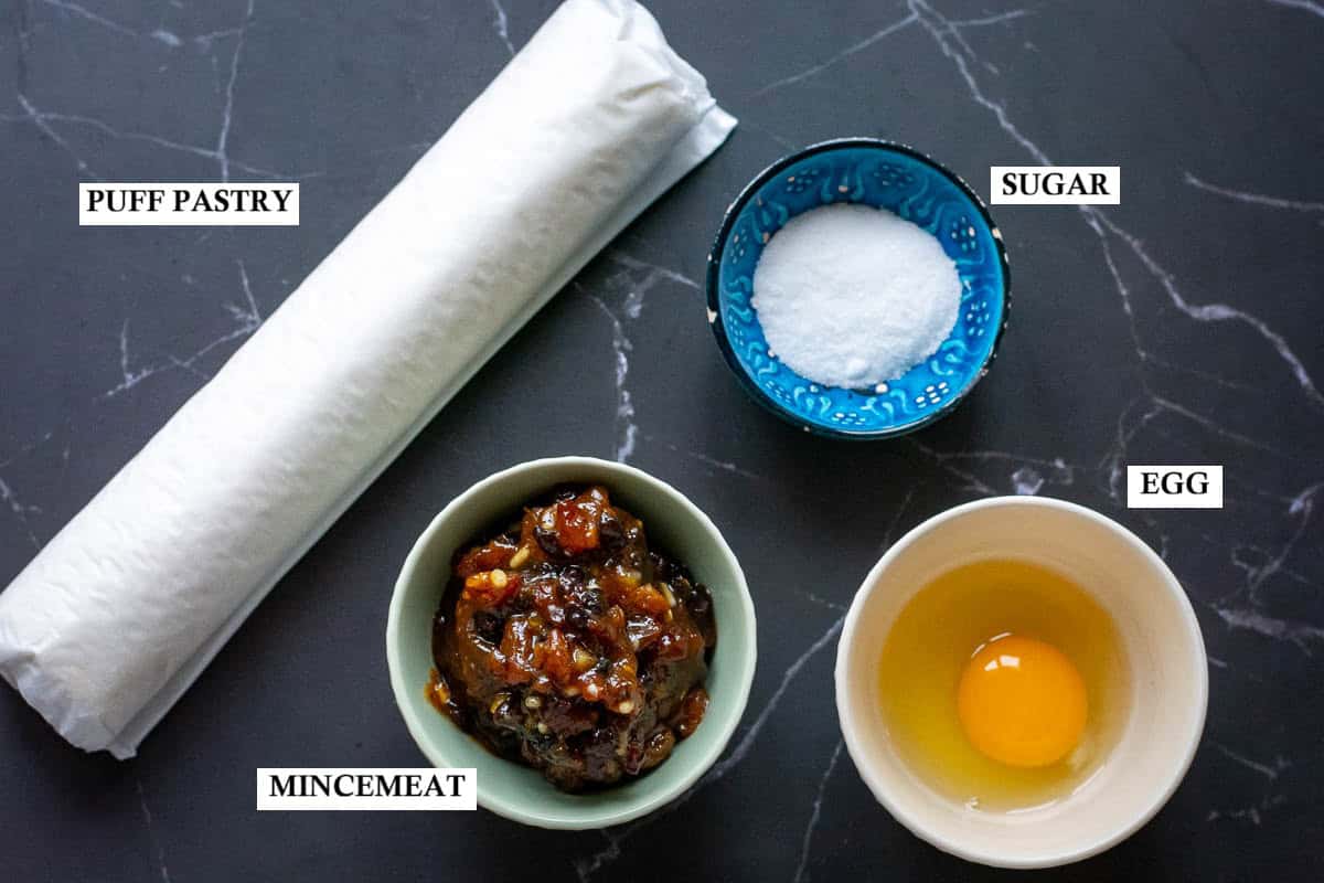 4 ingredients for puff pastry mince pies on a dark surface.
