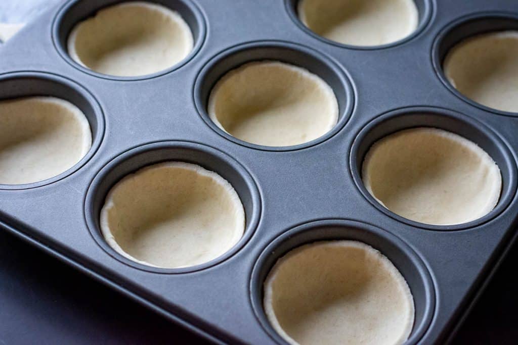 A 12-hole muffin tin lined with puff pastry discs.