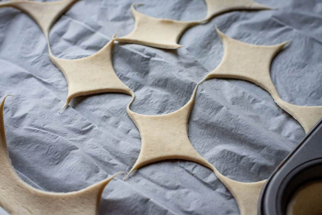 Puff pastry scraps in diamond shapes on a parchment paper.
