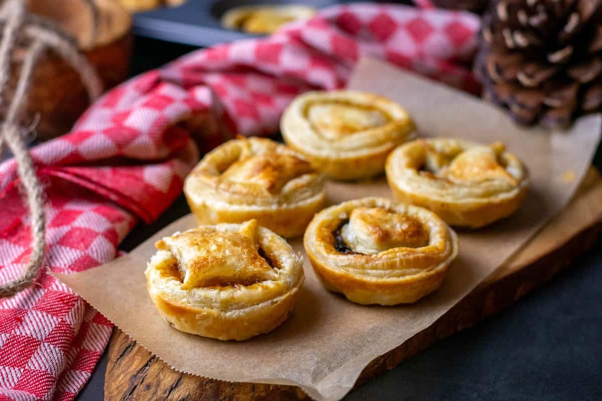 5 puff pastry mince pies arranged on a decorative wooden board.