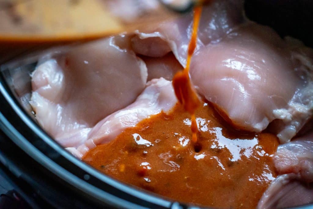 Pouring apricot sauce over the chicken thigh in a slow cooker.