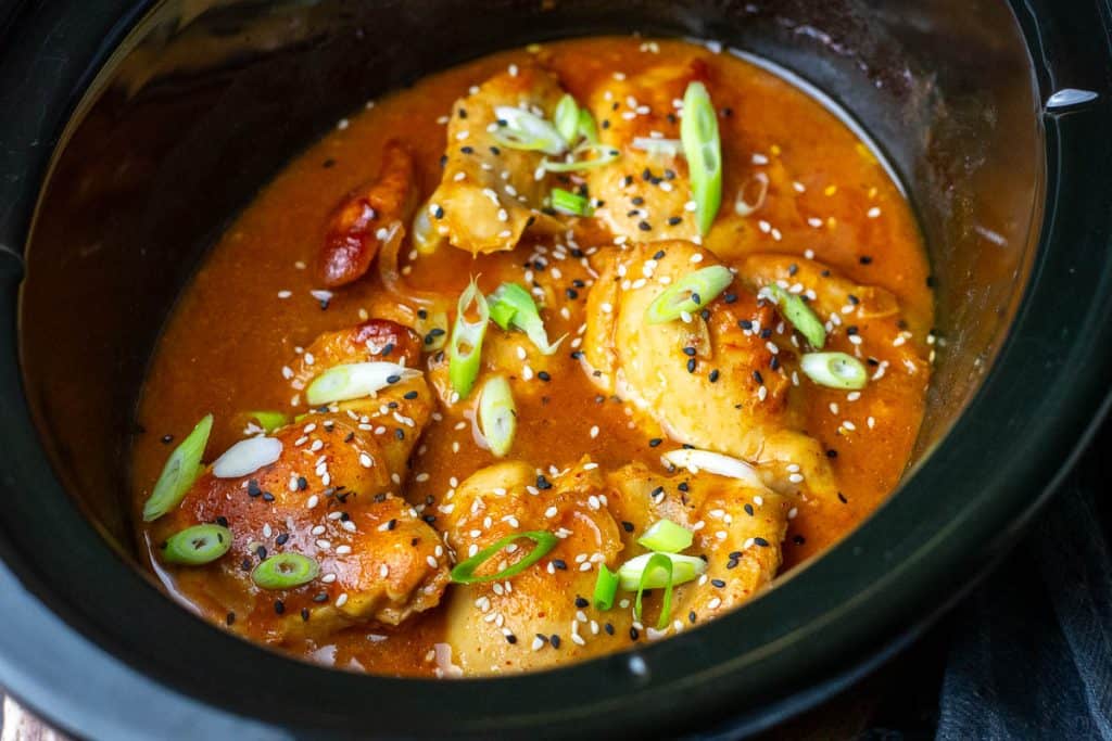 Slow cooker apricot chicken in a slow cooker bowl garnished with spring onions and sesame seeds.