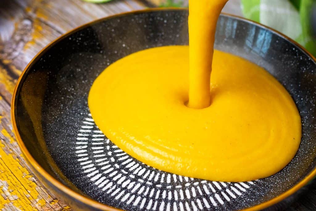 Pouring creamy carrot and parsnip soup into a black bowl.