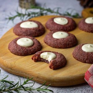 Sourdough Red Velvet Thumbprint Cookies on a wooden board with one bitten into.