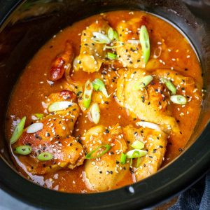 Slow cooker apricot chicken in a slow cooker bowl garnished with spring onions and sesame seeds.