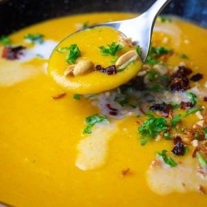 Curried Carrot and Parsnip Soup With Coconut Milk and various toppings being eaten with a spoon.