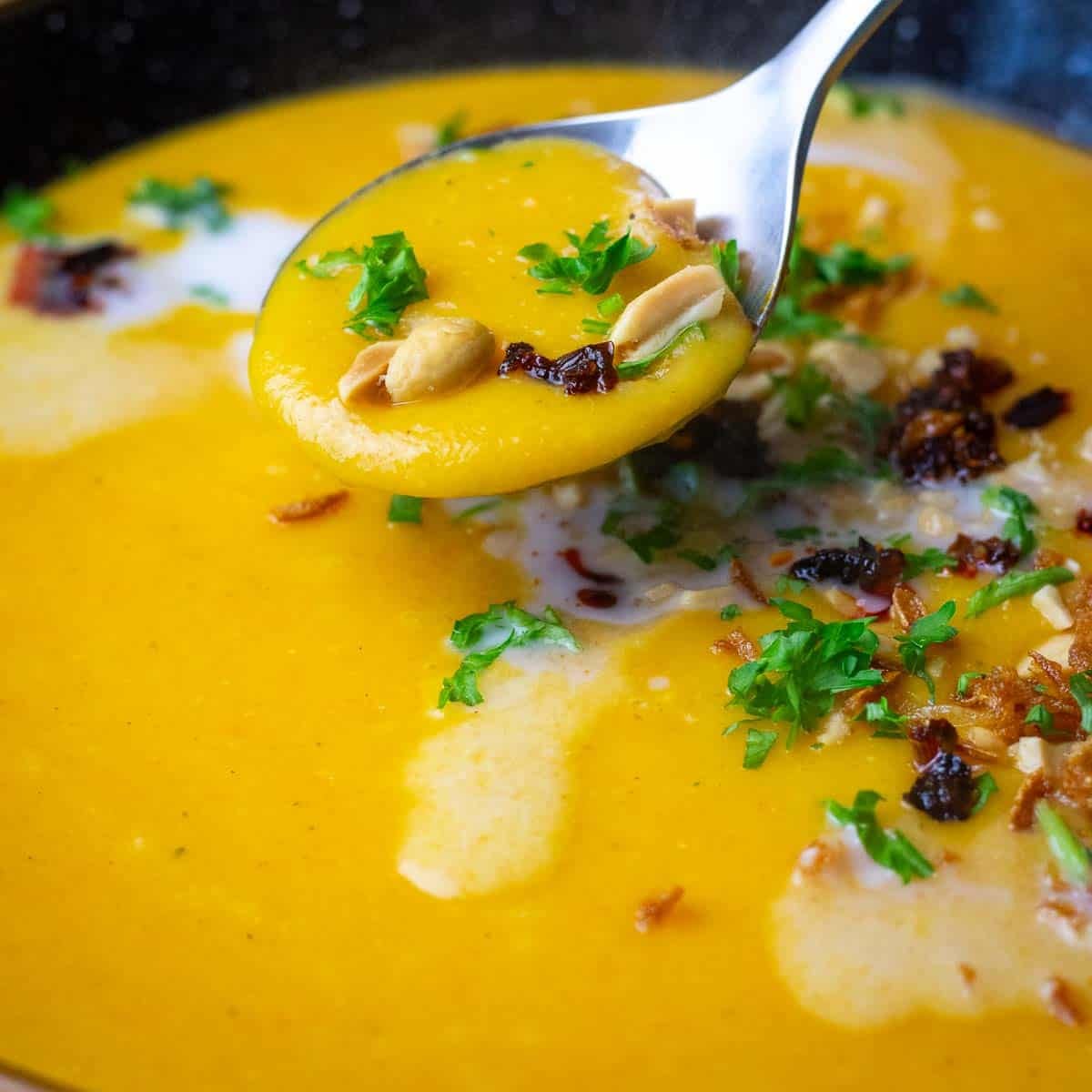 Curried Carrot and Parsnip Soup With Coconut Milk and various toppings being eaten with a spoon.