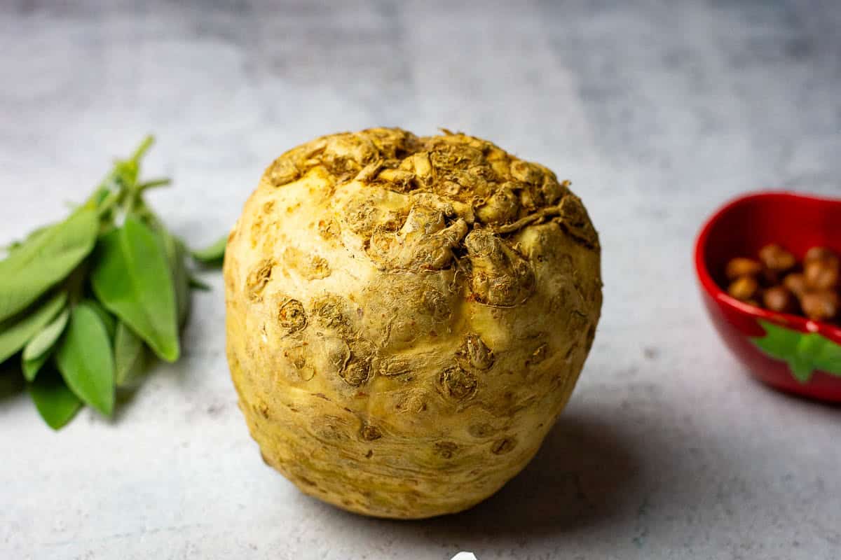 A whole celeriac on a light kitchen surface next to sage and hazelnuts.