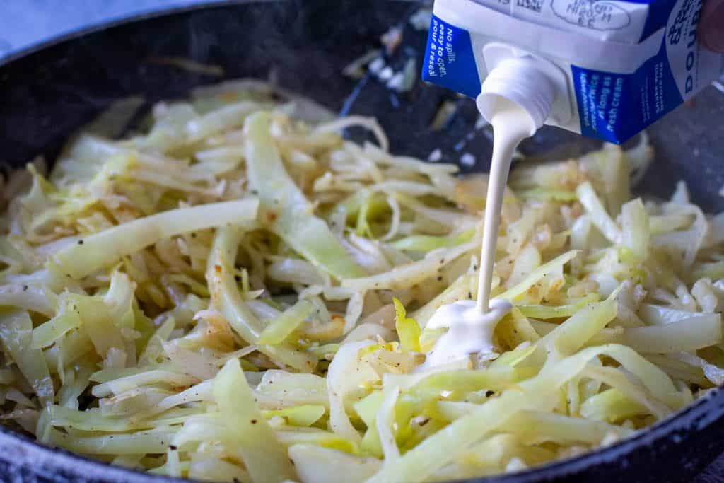 Pouring cream into sauteed cabbage.