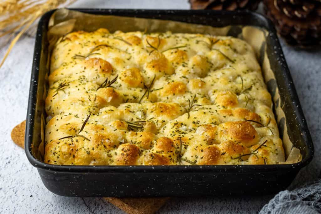 Baked sourdough focaccia with rosemary in a high-rimmed baking tray.
