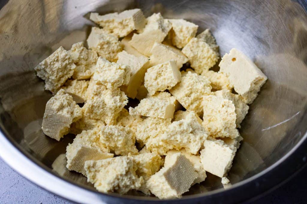 Broken up firm tofu pieces in a large metal bowl.