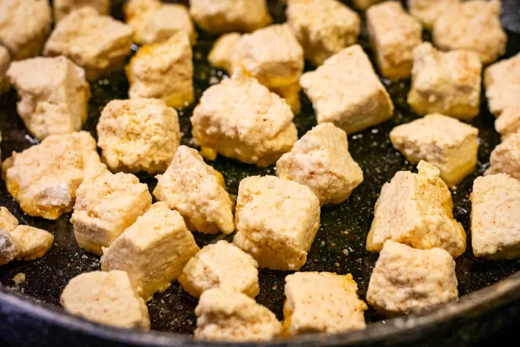 Cornflour coated tofu frying in a pan.