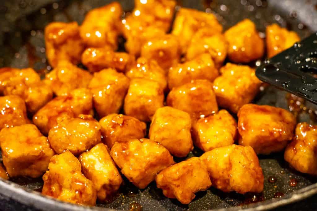 Crispy tofu coated in teriyaki sauce in a frying pan.