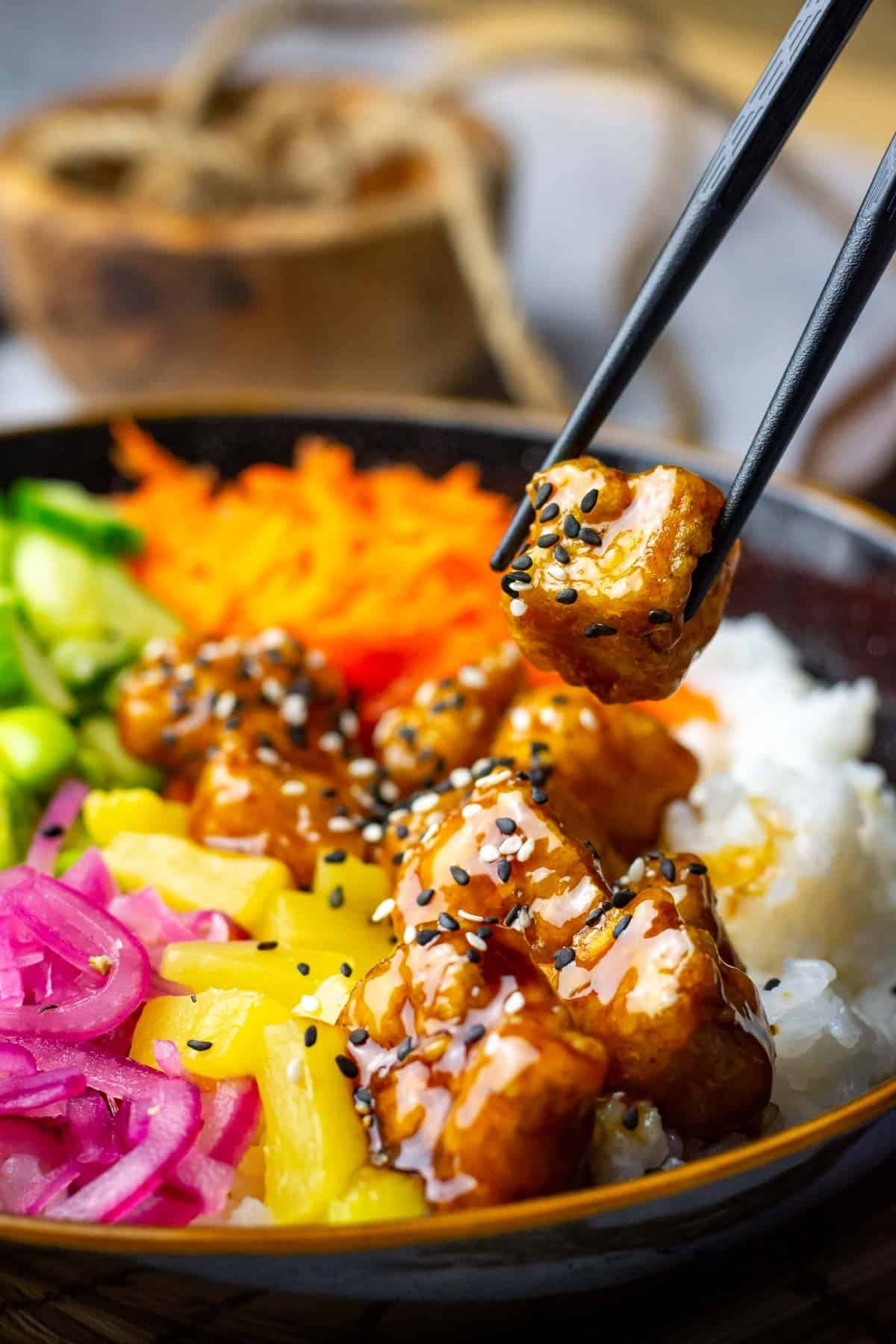 A piece of teriyaki tofu being picked up from a poke bowl.