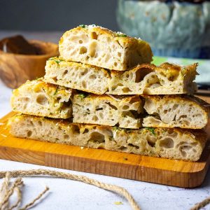 Garlic Butter Sourdough Focaccia cut into squares and stacked on a wooden board.