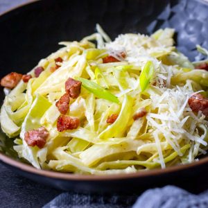 Creamy cabbage alfredo with pancetta in a black bowl.