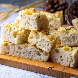 Beginner friendly Rosemary Sourdough Focaccia sliced into squares on a wooden board.
