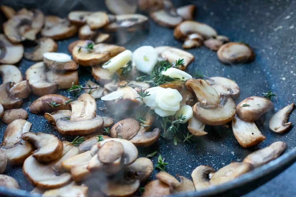 Sauteed mushrooms in a pan with garlic added on top.
