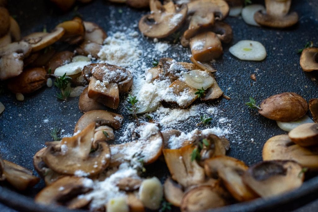 Flour sprinkled across the mushrooms in a frying pan.