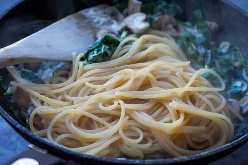 Cooked spagehtti added to the mushroom and spinach pan.