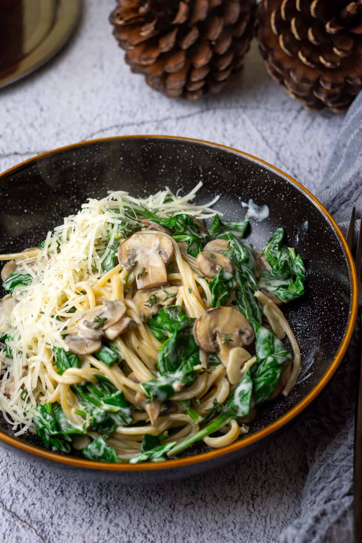 Mushroom and Spinach Pasta with Creme Fraiche Sauce with parmesan on top in a black bowl.