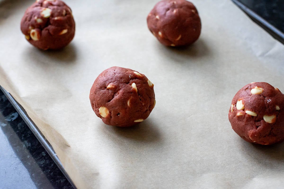 Balls of sourdough cookie dough on a parchment paper lined baking sheet.
