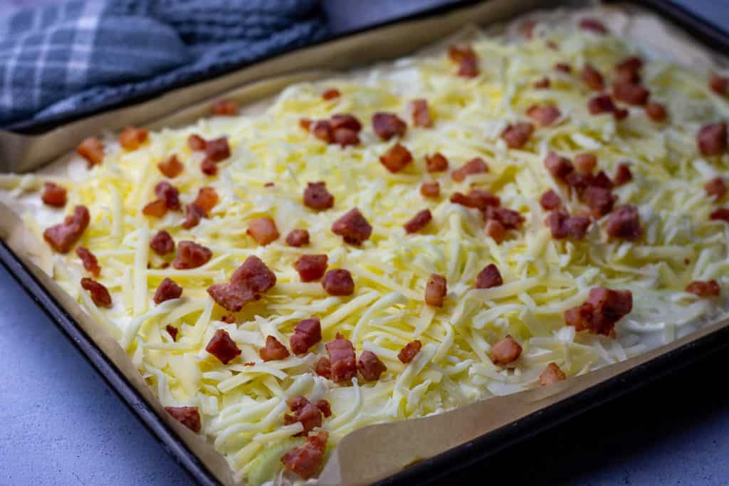 Cheese and crispy bacon lardons added on top of sourdough flammkuchen.