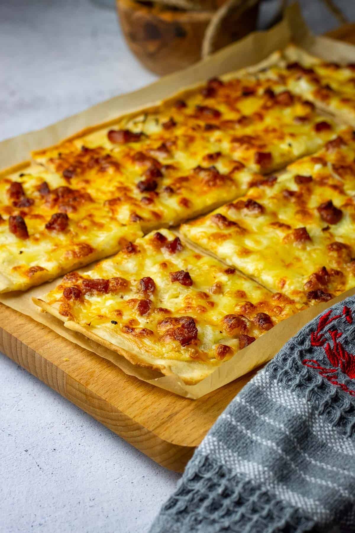 Sourdough Flammkuchen, also known as Tarte Flambee, cut into squares on a wooden board.