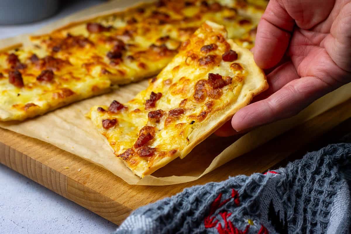 A slice of Alsatian sourdough flammkuchen eing picked up from the board.