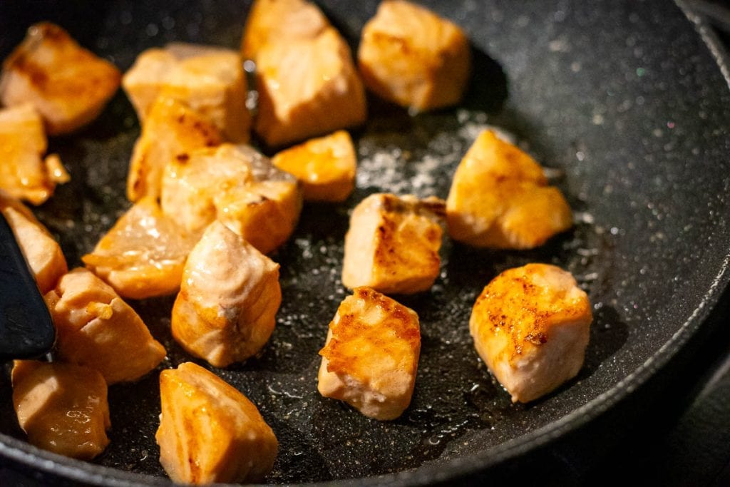 Seared Salmon cubed cooking in a frying pan.