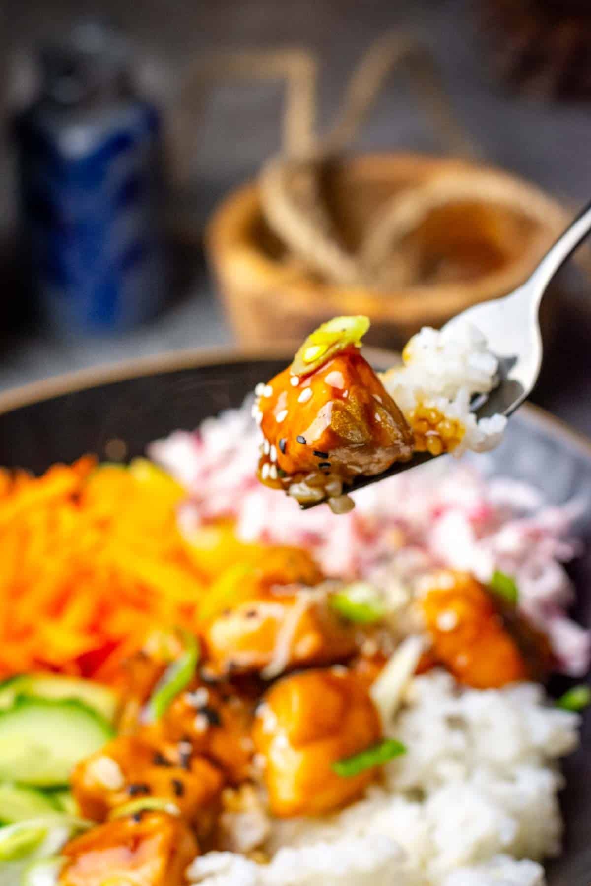 A piece of teriyaki salmon being icked up from a poke bowl.