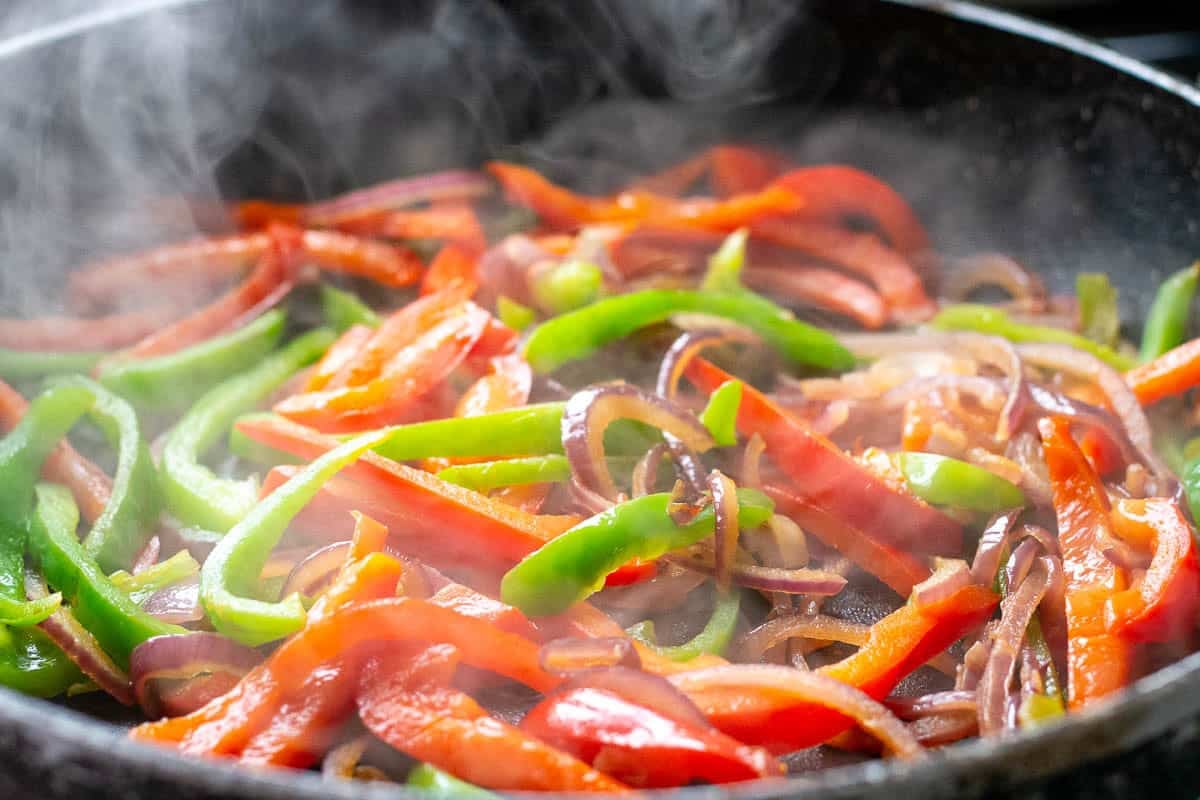 Onions and bell peppers frying in a pan.
