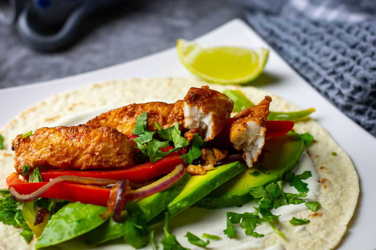 Blackened fish fajita filling on top of the tortilla wrap with a lime wedge on the side.