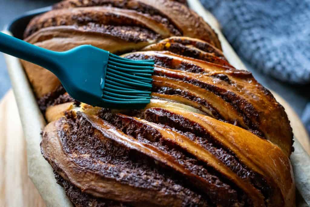 Brushing baked sourdough babka with sugar syrup.