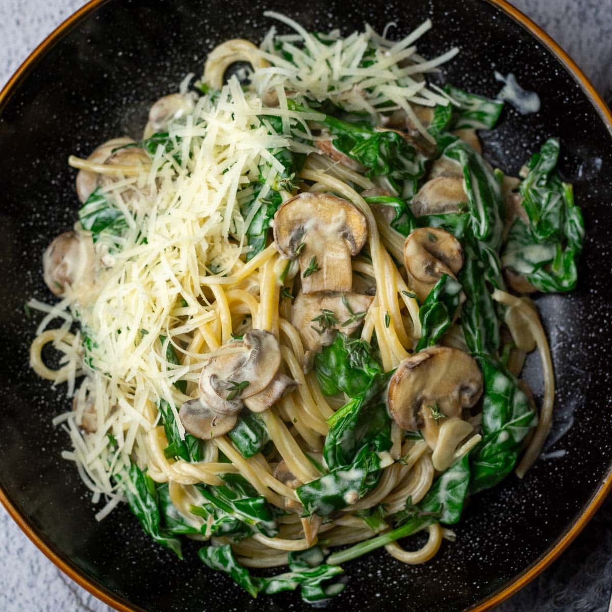 Mushroom and Spinach Pasta with Creme Fraiche Sauce with parmesan on top in a black bowl.