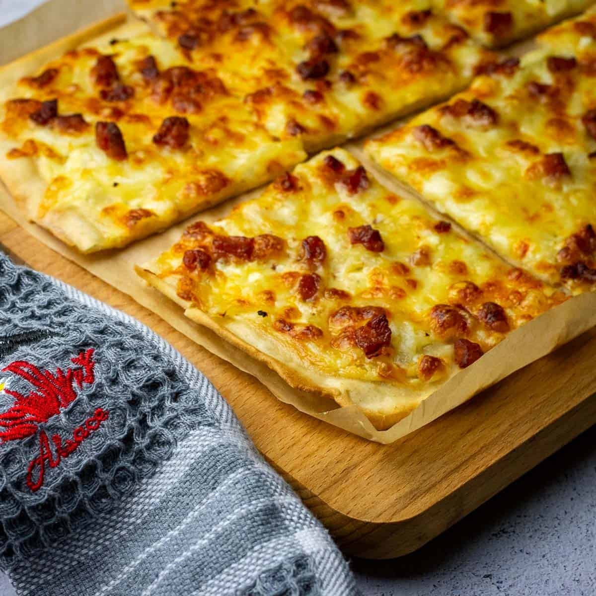 Sourdough Flammkuchen, also known as Tarte Flambee, cut into squares on a wooden board.