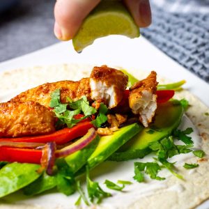 Lime juice being squeezed onto blacked fish fajitas on a white plate.