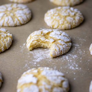 Sourdough Lemon Crinkle Cookies on a baking sheet, one bitten into.
