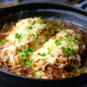 Baked French Onion Chicken breasts in a cast iron pan under a blanket of melted cheese.