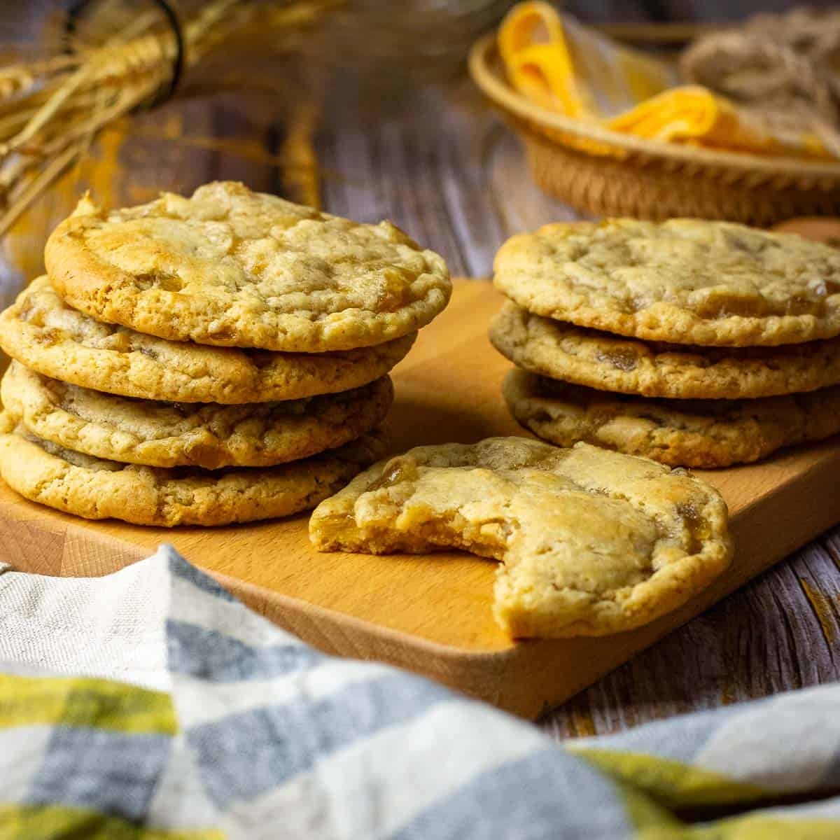Stacks of soudough ginger cookies on a wooden board with one sourdough cookie missing a bite.