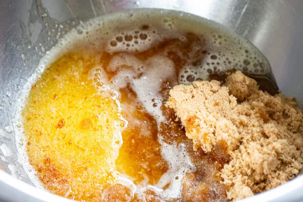 Brown butter poured over two types of sugar in a large mixing bowl.