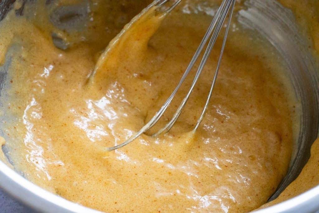Wet ingredeints being mixed with a balloon whisk.