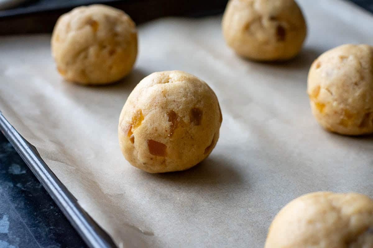 Balls of sourdough ginger cookie dough on a parchment paper lined baking sheet.