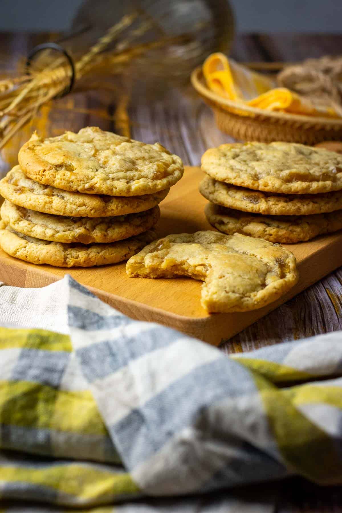 Stacks of soudough ginger cookies on a wooden board with one sourdough cookie missing a bite.