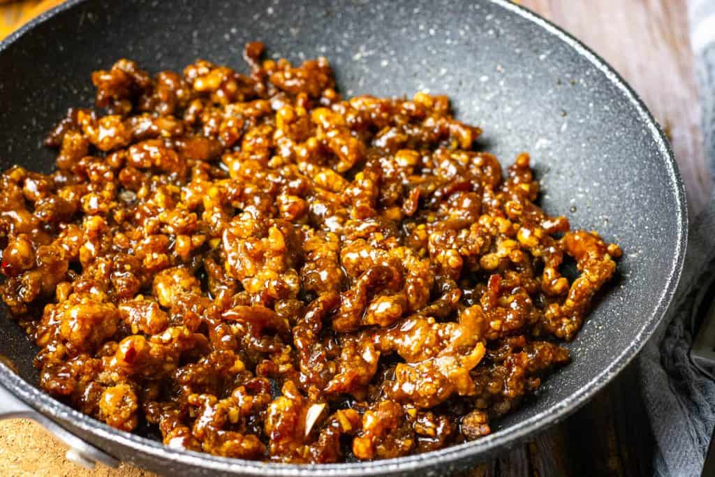 Crispy beef coated in teriyaki sauce in a frying pan.