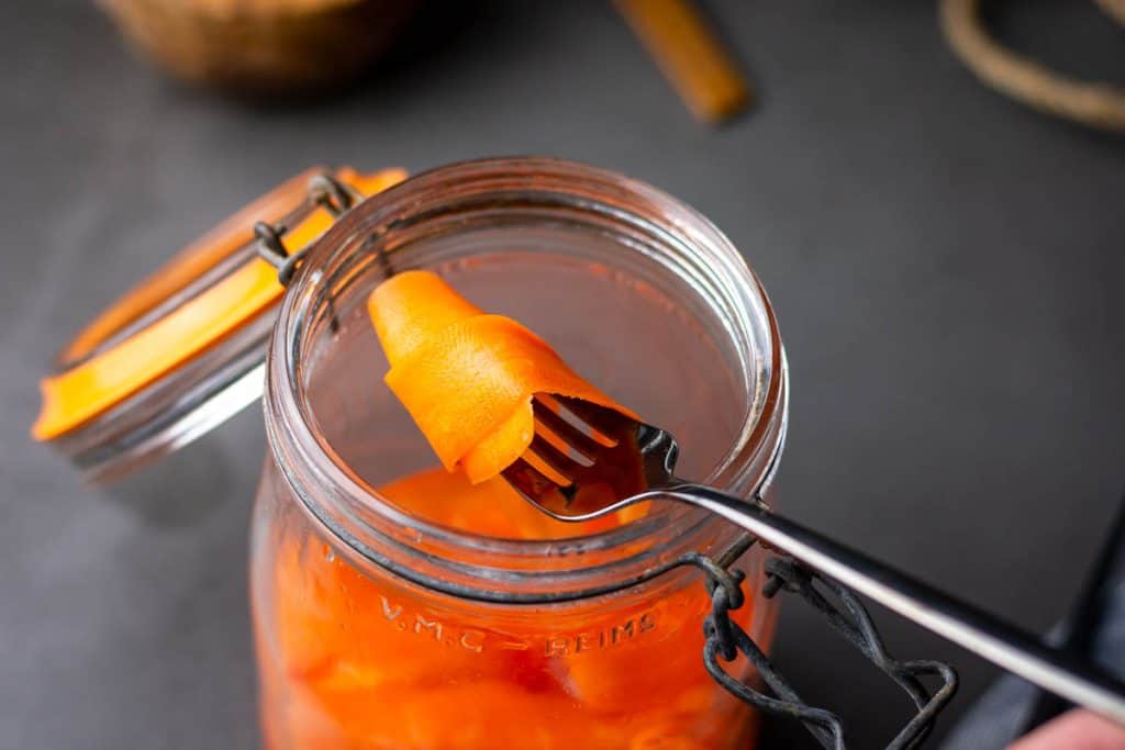 Pickled carrot ribbons being picked out of the ar with a fork.